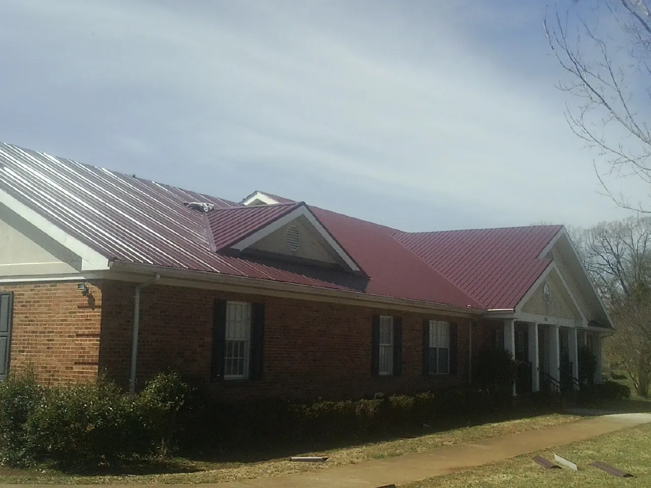 Red metal roof with gabled entries on a long brick building, from a Hail Damage Roof Repair job in Tecate