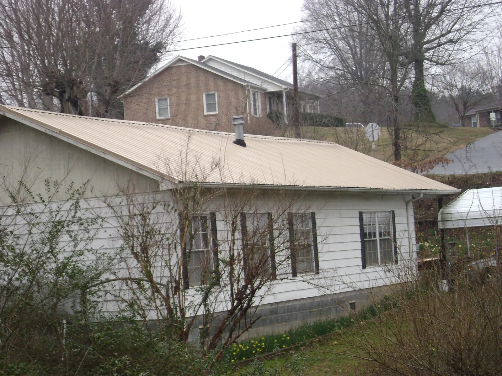 Tan metal roof on a white sided house set into a hillside — Commercial Roofing by Roofing Brothers in Tecate